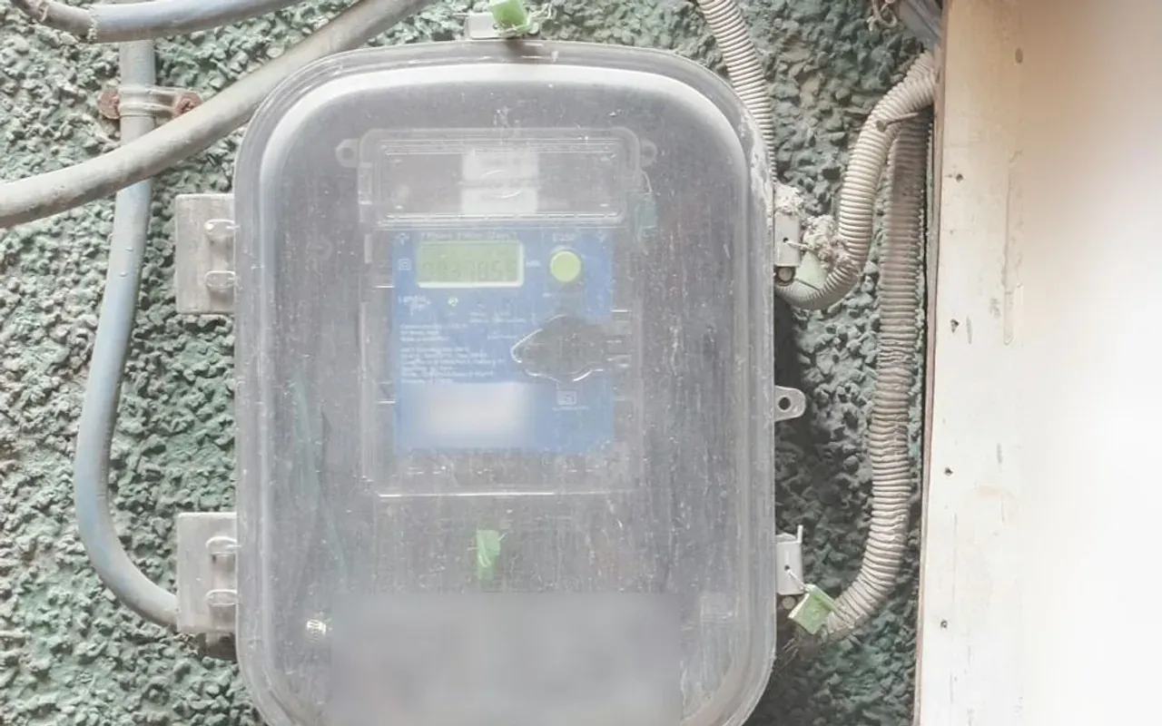 Digital electricity meter in a clear box on a textured wall